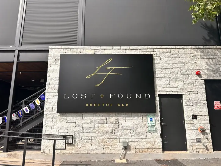 Sign on side of Lost and Found Rooftop Bar which is a black building with tan bricks.